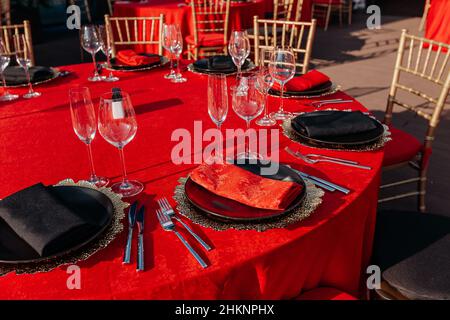 Tavolo per gli ospiti per banchetti in stile nero, rosso e oro. Allestimento cena elegante e di lusso: Arredamento, tovaglie, piatti, bicchieri, tovaglioli, posate. Compleanno a tema o festa di nozze Foto Stock