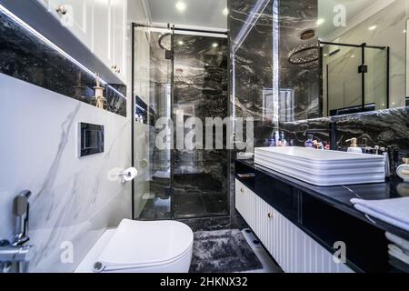 Bagno e wc in elegante versione in bianco e nero. Pavimenti con motivi in marmo bianco e nero. Lavandino con specchio, wc e doccia. Foto Stock