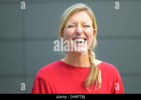 Donna bionda che si diverte con bubblegum o gomma da masticare con occhi larghi contro una parete grigia Foto Stock