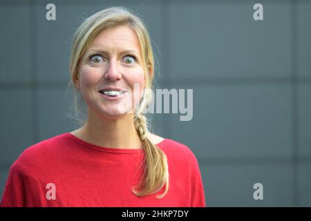 Donna bionda che si diverte con bubblegum o gomma da masticare con occhi larghi contro una parete grigia Foto Stock