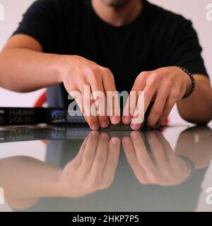 Giovane uomo mescolando e trattando carte su un tavolo da cucina riflettente in vetro a casa; gioco notte di famiglia. Foto Stock