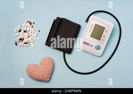 Un dispositivo per misurare la pressione, tonometro su sfondo medico blu, cuore a maglia e pillole. Cefalea, trattamento dell'ipertensione e ipotensione. Foto Stock