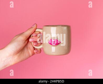 Concetto di giorno di San Valentino. Tazza con tenuta di mano con immagine delle labbra su sfondo rosa. Regalo a donna per la giornata di San Valentino. Foto di alta qualità Foto Stock