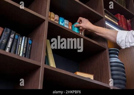 Mano dell'uomo che prende il libro dallo scaffale della biblioteca o che mette indietro. Possibilità di prenotare in libreria a casa o in ufficio. Foto di alta qualità Foto Stock