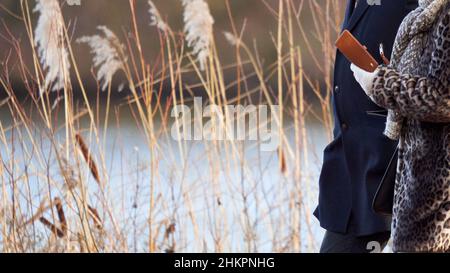 Uomo e donna che camminano insieme di fronte ad un lago. La mano tiene ebook. Coppia in abiti invernali. Foto Stock