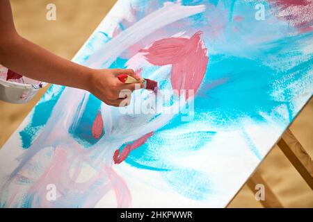 Pittore dilettante che disegna un'immagine su tela bianca al laboratorio di arte all'aperto. Donna artista mani con pittura pennello nuovo quadro, esercizio di arte all'aperto Foto Stock