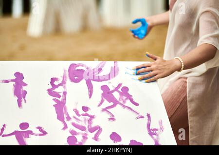 Donna mano spalmabile vernice blu su tela, espressione d'arte all'aperto festival d'arte. Espressione di pittura a goccia, sbavatura e vernice splattering su bianco ca Foto Stock