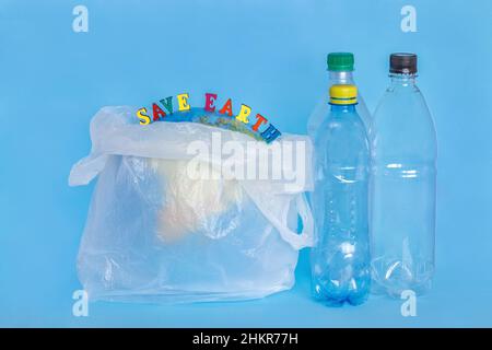 Iscrizione SAVE EARTH, bottiglie di plastica, terra astratta in sacchetto di polietilene, sfondo blu. Concetto problema di ecologia del piano di inquinamento ambientale Foto Stock