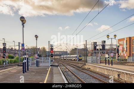 La fine di una piattaforma ferroviaria dove i binari scompaiono in lontananza. Ci sono luci di segnalazione sulle piattaforme e un cielo con le nuvole è sopra. Foto Stock