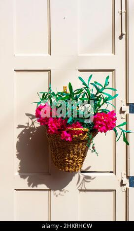 Cestino di vimini con fiori appesi su una porta di legno Foto Stock