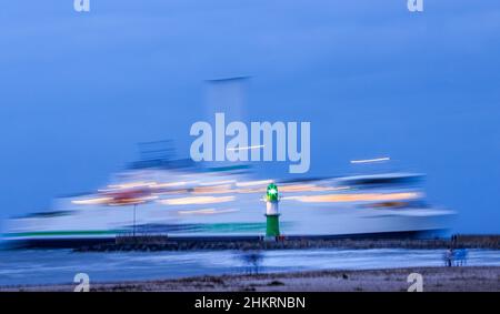 05 febbraio 2022, Meclemburgo-Pomerania occidentale, Warnemünde: Alcune passeggine osservano la sera il traghetto Scandlines 'Copenhagen' che entra nel porto di Rostock. (Foto a lunga esposizione) il clima invernale secco e freddo attrae ancora turisti e turisti alla spiaggia dopo il tramonto, nonostante i forti venti. Foto: Jens Büttner/dpa-Zentralbild/dpa Foto Stock