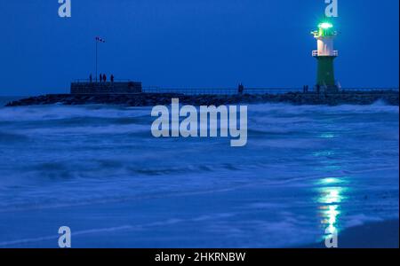 05 febbraio 2022, Meclemburgo-Pomerania occidentale, Warnemünde: Il faro su uno dei moli all'ingresso del canale marittimo di Rostock lampeggia in serata. Il clima invernale secco e freddo attira ancora turisti e visitatori di giorno alla spiaggia anche dopo il tramonto, nonostante il vento feroce. Foto: Jens Büttner/dpa-Zentralbild/dpa Foto Stock