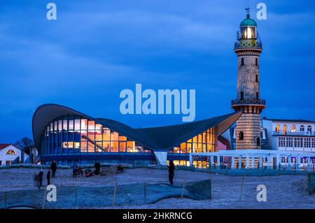 05 febbraio 2022, Meclemburgo-Pomerania occidentale, Warnemünde: Lo storico faro dietro il cosiddetto Teepott di Warnemünde emette i suoi segnali luminosi di sera. Il clima invernale secco e freddo attira ancora turisti e visitatori di giorno alla spiaggia anche dopo il tramonto, nonostante il vento feroce. Foto: Jens Büttner/dpa-Zentralbild/dpa Foto Stock