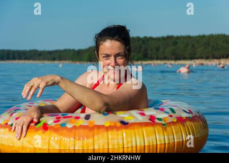 Giovane donna carina con cerchio gonfiabile colorato nuota nelle acque blu del mare in una calda giornata di sole, ciambella per nuotare, estate spiaggia vaca Foto Stock