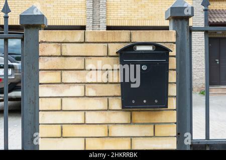 Mailbox di una casa privata, una mailbox in metallo nero installato su una recinzione in mattoni di una casa residenziale privata. Foto Stock