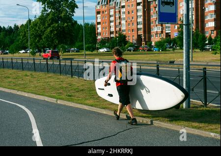 Un uomo sportivo cammina attraverso la città e porta in mano una scheda SUP. Foto Stock