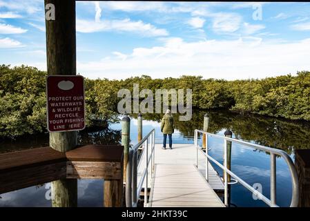 Una vista posteriore di una donna matura di 50-60 anni con lunghi capelli grigi e con un parka in piedi su un bacino galleggiante nella riserva di Ponce Inlet, Florida Foto Stock