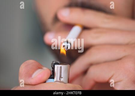 Primo piano di un giovane uomo che illumina e fuma sigaretta. Dipendenza da fumo e cattivo concetto di abitudine Foto Stock