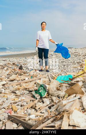 Giovane donna volontaria sulla spiaggia piena di spazzatura Foto Stock