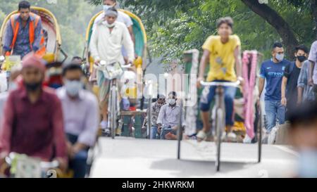 Persone che camminano o cavalcano risciò sul loro modo di lavorare nella corsa mattutina a Dhaka martedì 12 luglio. Il Bangladesh sta attraversando un'impennata di COVID-19, con un record di 13768 casi lunedì 12 luglio. Il 14 luglio, le restrizioni di blocco saranno attenuate per nove giorni per le celebrazioni Eid-ul-Azha. Foto Stock