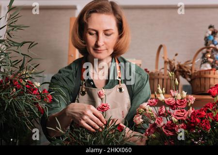 Bella donna fiorista che fa un bouquet regalo di rose. Ambiente di lavoro fiorista. Concetto di piccola impresa. Vista frontale. Fiori e accessori. Focu selettivo Foto Stock