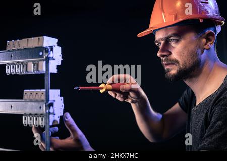 Un elettricista maschio lavora in un quadro elettrico con un cavo di collegamento elettrico. Foto Stock