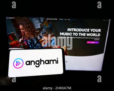 Persona che tiene il cellulare con il logo della piattaforma di streaming di musica araba Anghami sullo schermo di fronte al sito web aziendale. Mettere a fuoco sul display del telefono. Foto Stock