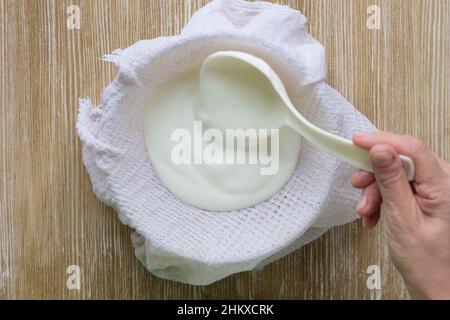 Fare la mano della donna dello yogurt greco mettendolo usando il cucchiaio della cucina sull'asciugamano del waffle per essere spessa sullo sfondo di legno Foto Stock