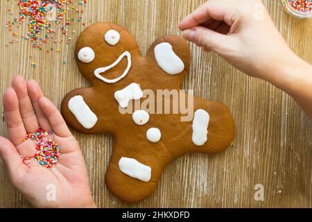 Biscotto di pan di zenzero al forno decorato con palle multicolore da donna a mano sullo sfondo di legno Foto Stock