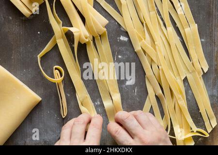 Le mani della donna preparano i noodles crudi per asciugare sulla polvere dalla superficie di legno della farina Foto Stock