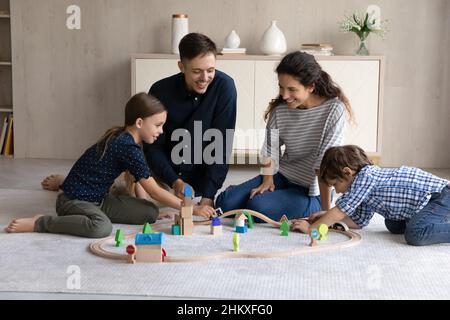 Felici genitori e due bambini che giocano con la ferrovia in legno Foto Stock