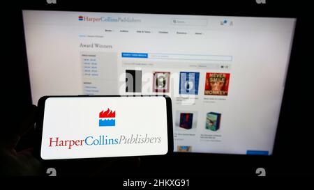 Persona che tiene il telefono cellulare con il logo della società americana HarperCollins Publishers LLC sullo schermo di fronte alla pagina web. Mettere a fuoco sul display del telefono. Foto Stock