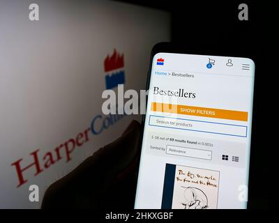 Persona che tiene smartphone con il sito web della società statunitense HarperCollins Publishers LLC sullo schermo di fronte al logo. Concentrarsi sul centro del display del telefono. Foto Stock