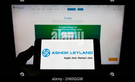 Persona che tiene il cellulare con il logo della società automobilistica indiana Ashok Leyland Ltd. Sullo schermo di fronte al sito web aziendale. Mettere a fuoco sul display del telefono. Foto Stock