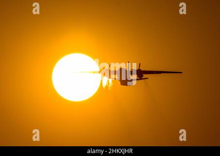 Silhouette di velivolo turboprop decollo durante il tramonto, vola ala attraverso il disco del sole. È visibile una traccia di aria calda proveniente dai motori Foto Stock