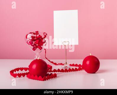 Cartolina del giorno di San Valentino. Nastro di cuori e candele a tavola su sfondo rosa. Vita morta in amore e stile romantico. Mockup. Foto di alta qualità Foto Stock