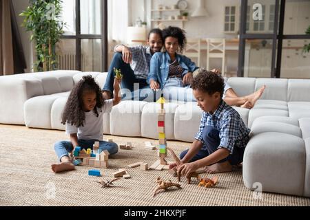 Genitori africani felici che guardano i bambini piccoli che giocano i giocattoli.
