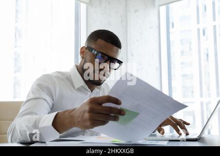 Responsabile africano americano serio in occhiali di stile che legge il documento corporativo Foto Stock
