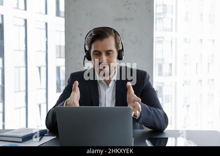 Uomo d'affari motivato in cuffie con microfono che parla durante la videochiamata Foto Stock