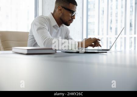 Un uomo d'affari focalizzato nel millenario nero che digita su un notebook in un ufficio moderno Foto Stock
