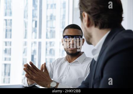 Serio impiegato africano impegnato in occhiali parlando con collega Foto Stock