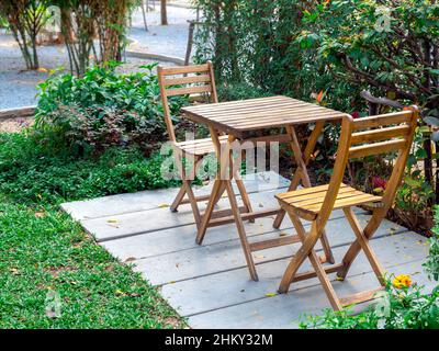 Tavolo da giardino all'aperto. Tavolo vuoto in legno e due sedie su pavimento in cemento su erba verde nel parco, nessuno. Foto Stock