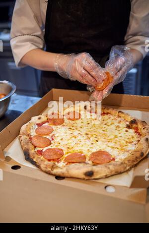 La macchina per la pizza mette gli ingredienti sull'impasto. Fare la pizza con salsiccia e salame Foto Stock