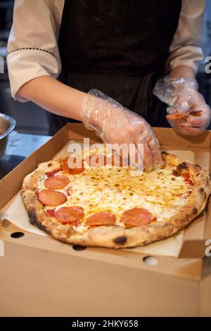 La macchina per la pizza mette gli ingredienti sull'impasto. Fare la pizza con salsiccia e salame Foto Stock