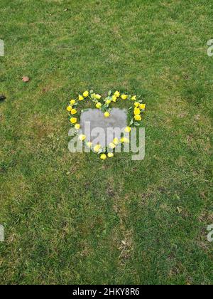 Fiori artificiali a forma di cuore si trovano accanto alla lapide nel cimitero. Foto Stock