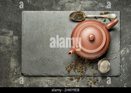 Teiera tradizionale cinese con tè verde che viene preparato su un vassoio di pietra nera, in piedi su uno sfondo di cemento nero. Vista dall'alto con spazio di copia per te Foto Stock