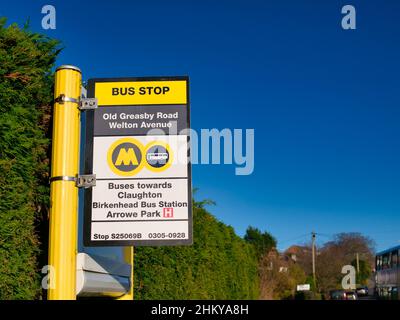 Fissato a un palo di metallo giallo, un cartello della fermata dell'autobus locale che mostra la posizione e le informazioni sul percorso. In una giornata di sole d'inverno. Foto Stock