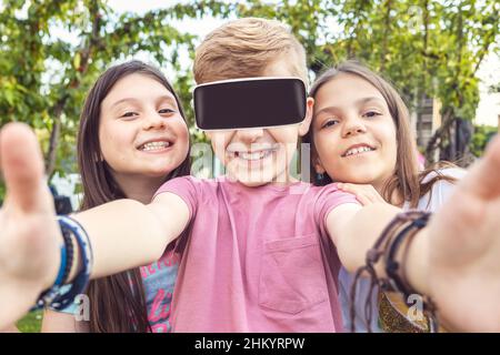 Felici i migliori amici i bambini che si divertono con i videogame vr nel mondo virtuale della metaversa durante la festa del cortile Foto Stock