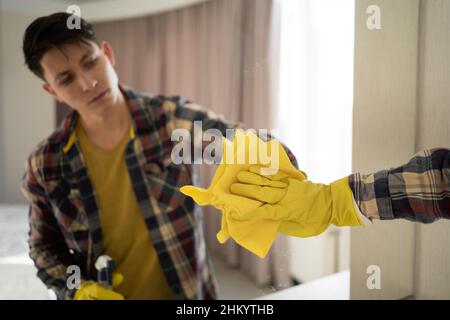 Un giovane hippster lava uno specchio a casa. uomo caucasico in guanti salviette specchio con spruzzatore detergente e panno, fa lavori di casa. mirr lavaggio uomo Foto Stock