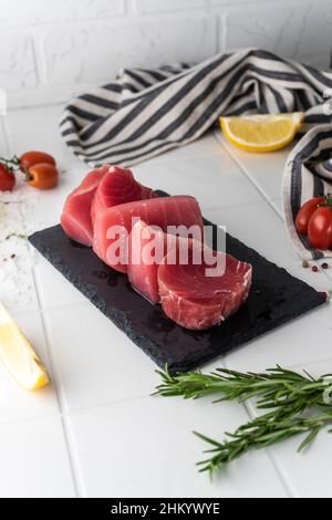 Bistecche di filetto di tonno fresco con spezie, verdure ed erbe su un piatto. Preparazione del tonno per la cottura. Foto di alta qualità Foto Stock